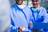 A surgeon and a nurse in an operating room congratulate a fellow surgeon on a successful surgical intervention performed with the help of a surgical cobot.